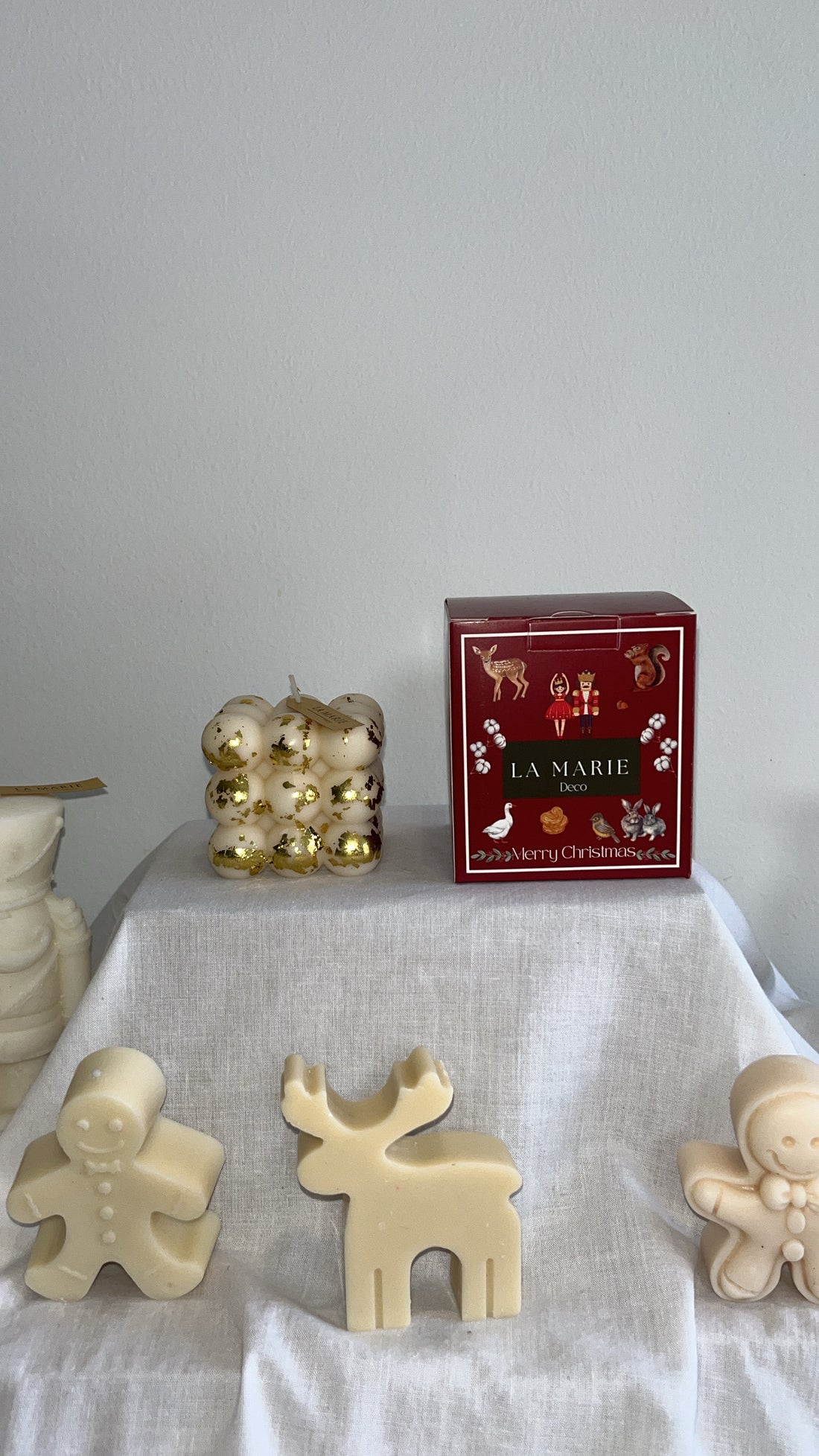 Cubo Abundancia de La Marie en dorado, junto a una caja roja y figuras de cera blanca sobre un mantel