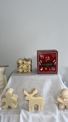 Cubo Abundancia de La Marie en dorado, junto a una caja roja y figuras de cera blanca sobre un mantel