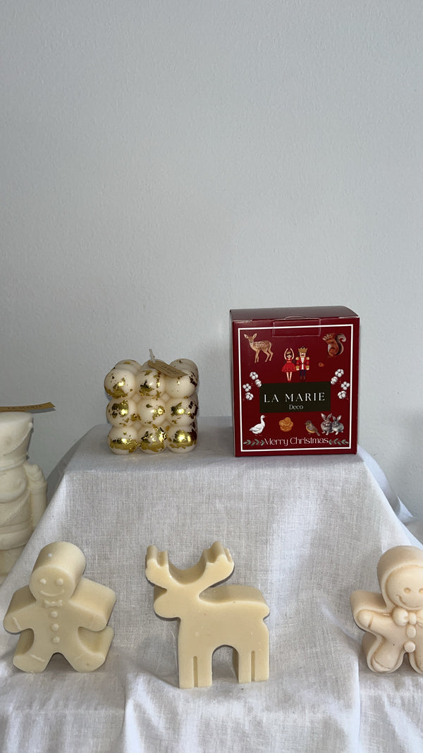 Cubo Abundancia de La Marie en dorado, junto a una caja roja y figuras de cera blanca sobre un mantel