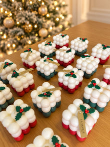 Cubos navideños de La Marie en filas sobre una mesa, en rojo y verde, con acebo y etiqueta dorada
