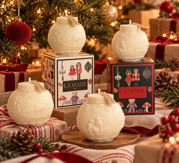 Velas esfera de El Milagro de Navidad de La Marie en crema, junto a sus cajas y adornos navideños