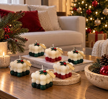 Cubos navideños de La Marie en rojo y verde sobre una mesa de centro, junto a ramas de pino, en una sala decorada para Navidad